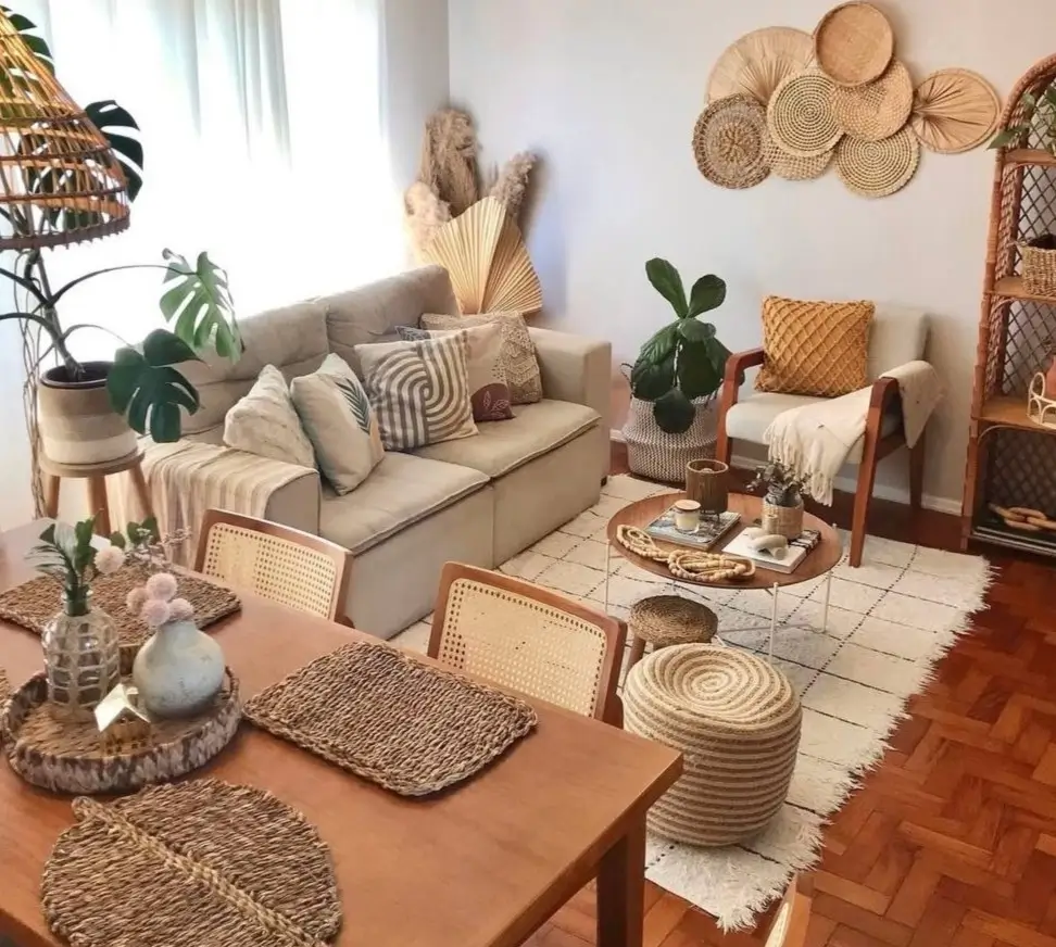 A neutral bohemian living room with a beige sofa, layered rugs, and a gallery wall of woven baskets and fans.