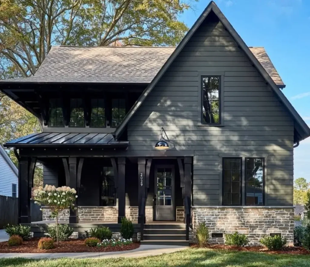 A modern cottage exterior with dark green siding, a stone foundation, and black trim on the porch and windows.