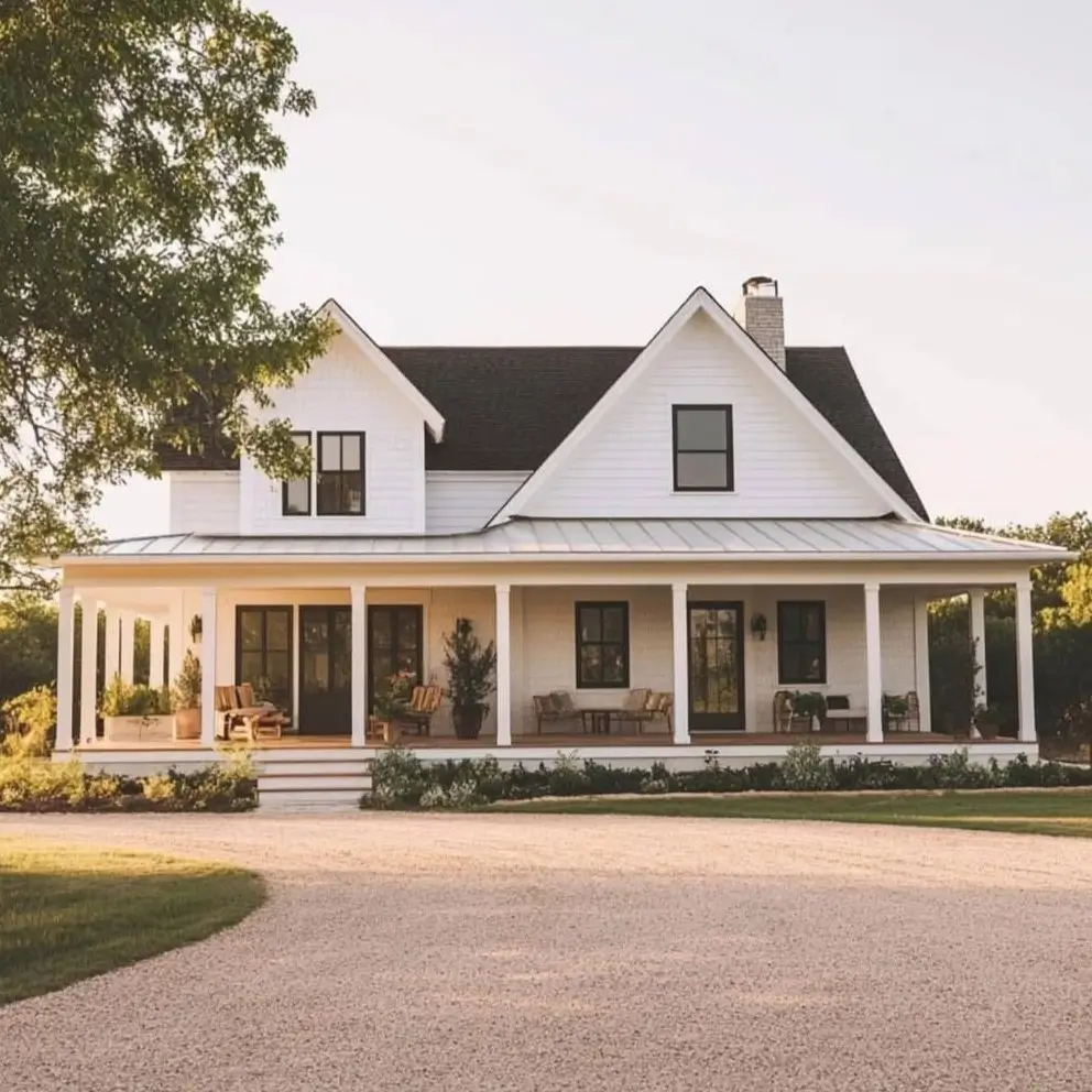 A modern white farmhouse with a dark roof and a large wraparound porch with comfortable seating areas.