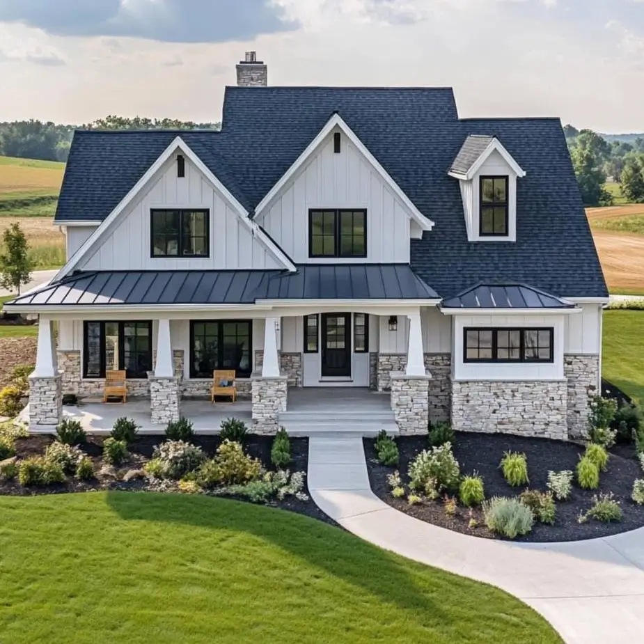 A modern white farmhouse with a dark roof and a stone veneer foundation, set on a manicured green lawn.