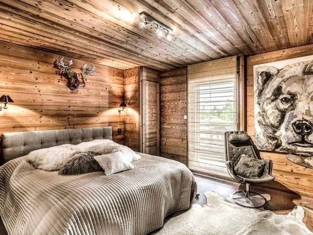 A modern rustic bedroom for couples with light wood paneling, a large contemporary painting of a bear, and a grey upholstered bed.