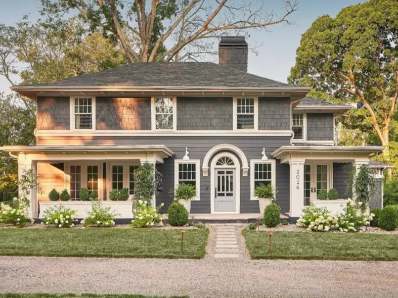 A symmetrical two-story cottage with dark gray siding, a central arched front door, and balanced landscaping.