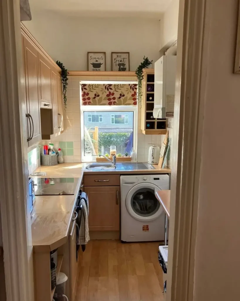 A narrow galley kitchen with light wood cabinets and a large window over the sink.