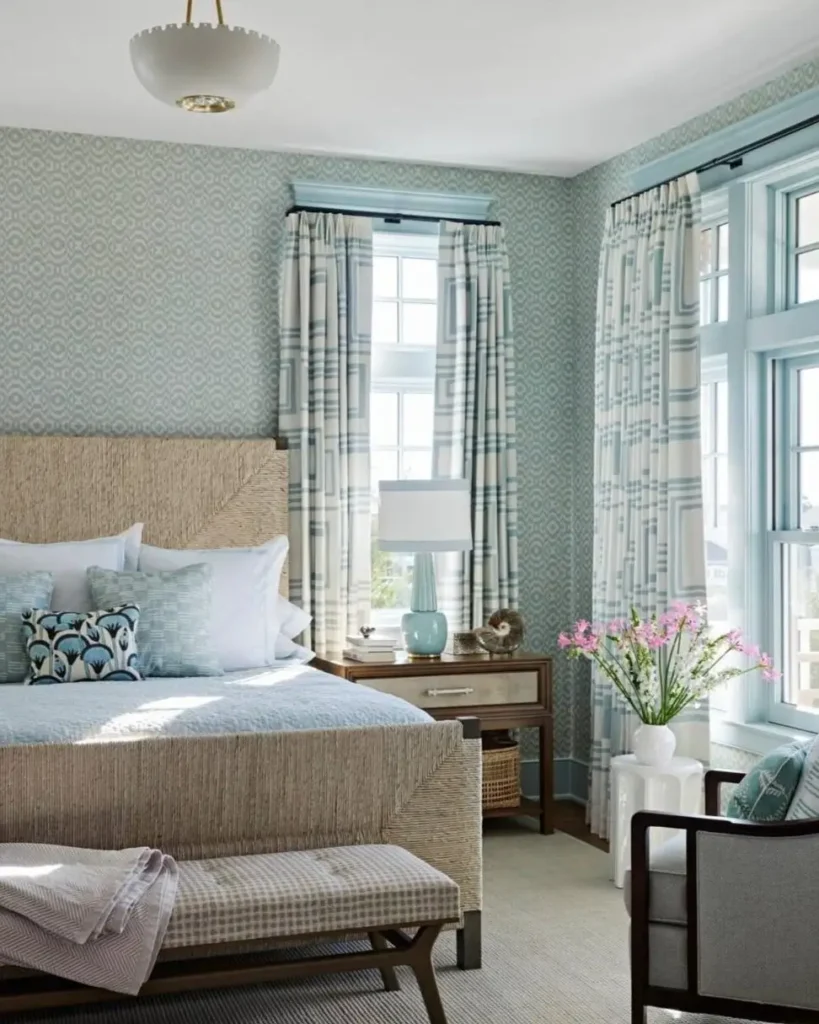 A sophisticated beach themed bedroom with a woven bed, light blue patterned wallpaper, and matching curtains.
