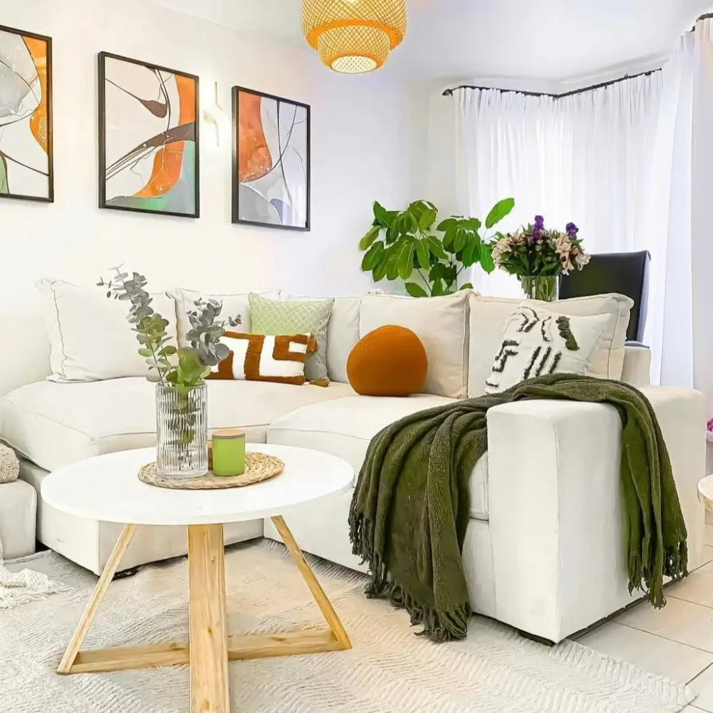 A bright living room with a white sectional sofa, a trio of modern abstract paintings, and an olive green throw.