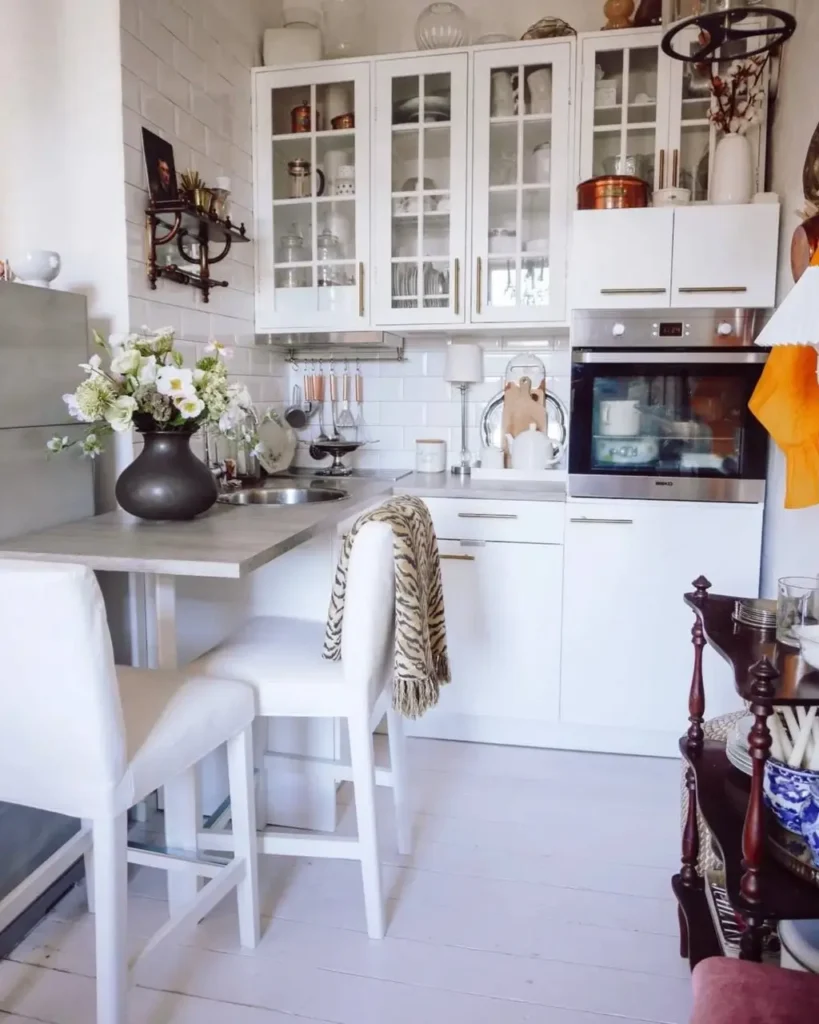 A tiny white kitchen with a wall-mounted dining bar and two white stools.