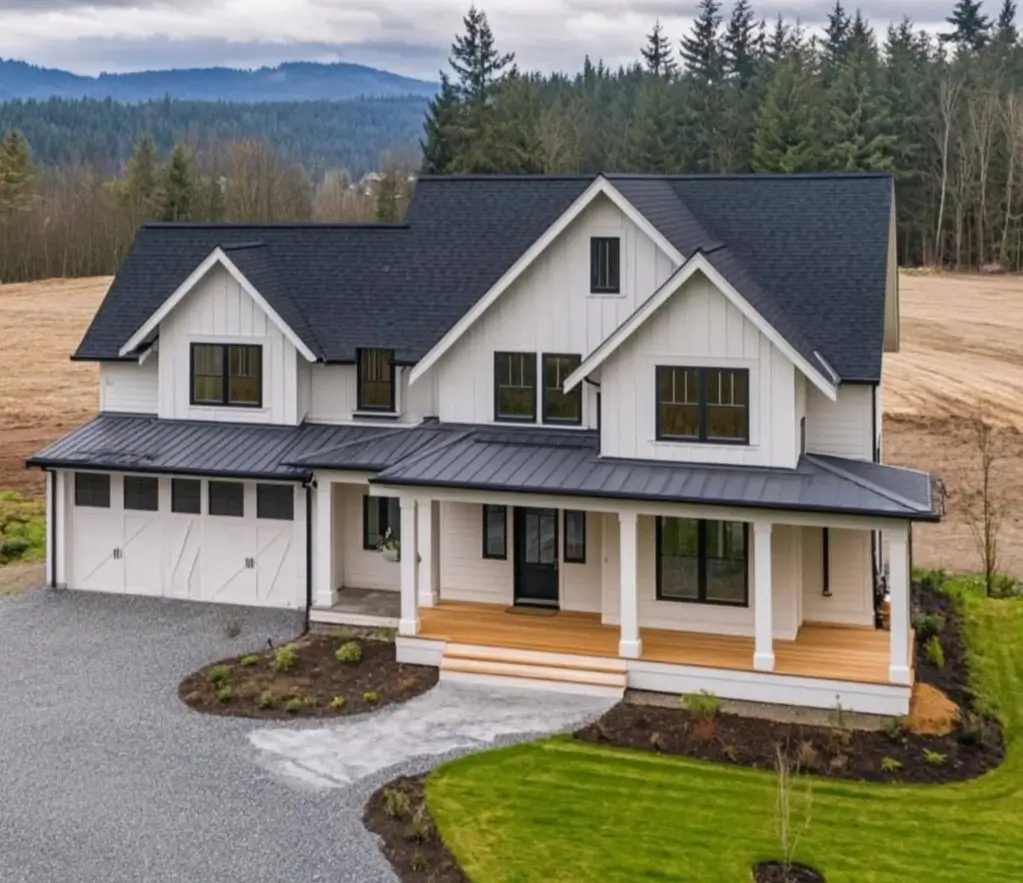 A modern white farmhouse featuring a natural wood porch floor, black trim, and white carriage-style garage doors.