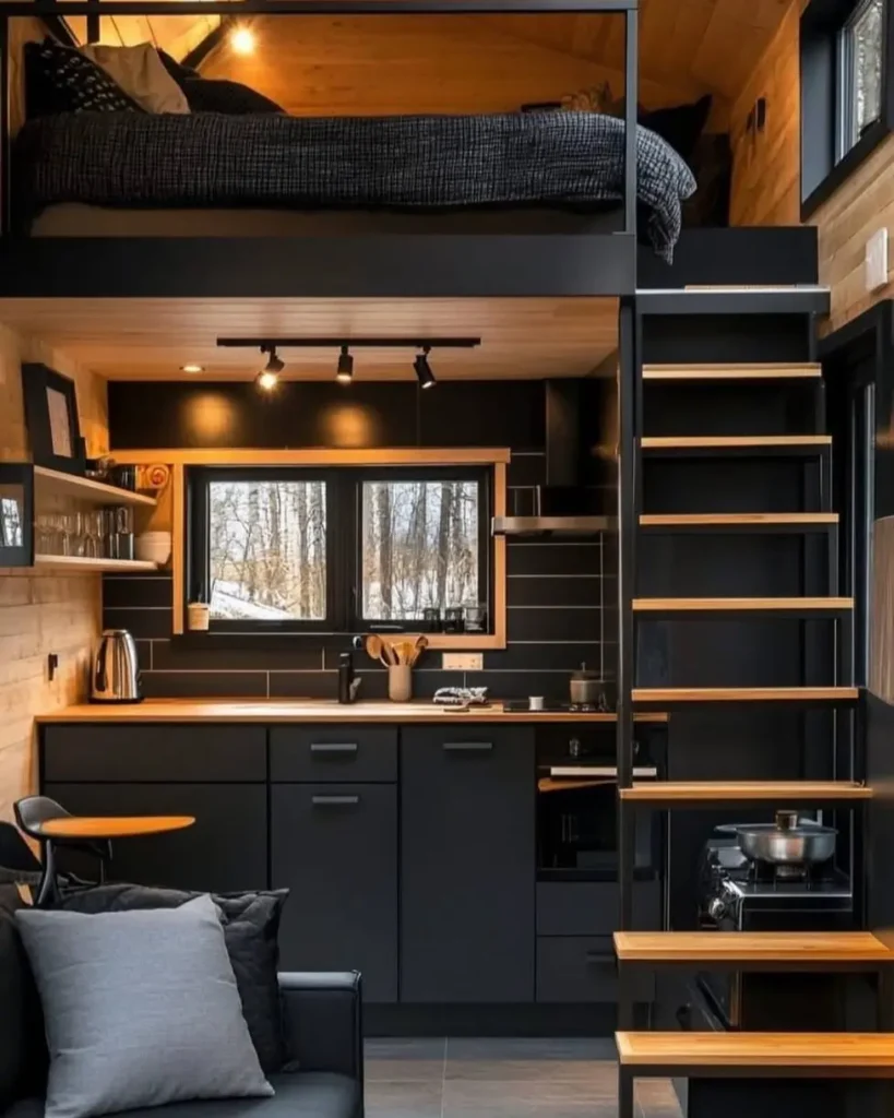 A tiny house kitchen with matte black cabinets and a wood countertop under a sleeping loft.