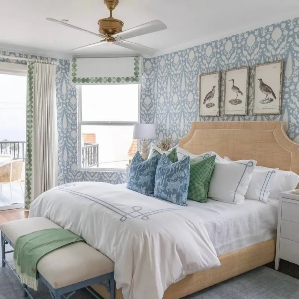 A coastal bedroom with a woven bed, blue patterned wallpaper, and a triptych of shorebird art above the headboard.