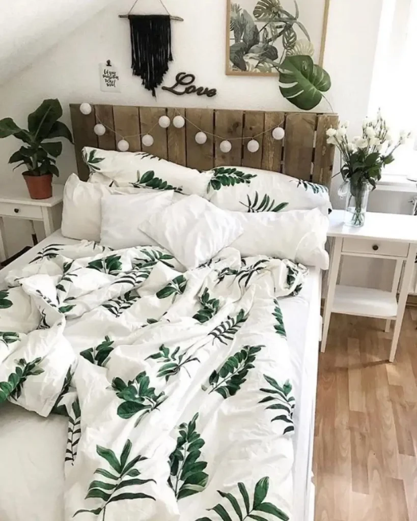 A bed with a white and green leaf-patterned duvet set against a rustic reclaimed wood headboard.