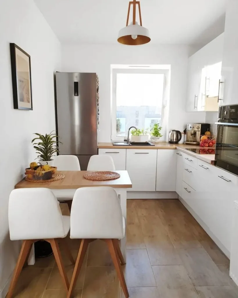 A small, modern eat-in kitchen with white cabinets and a wooden dining table.