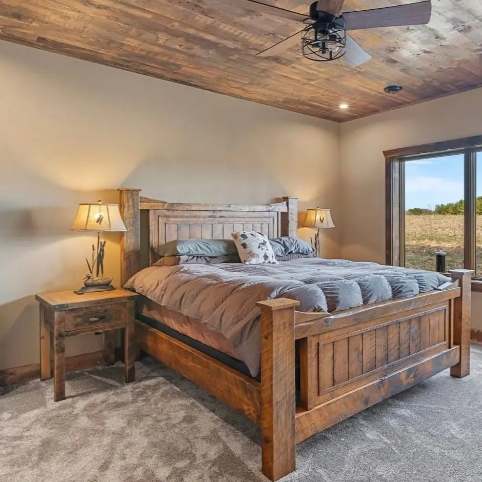 A country rustic bedroom featuring a reclaimed wood ceiling, a large wooden bed, and a picture window overlooking a field.