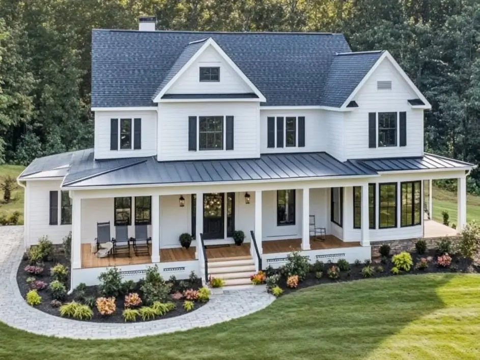 A modern white farmhouse with a wraparound porch and layered landscaping beds along a curved stone walkway.