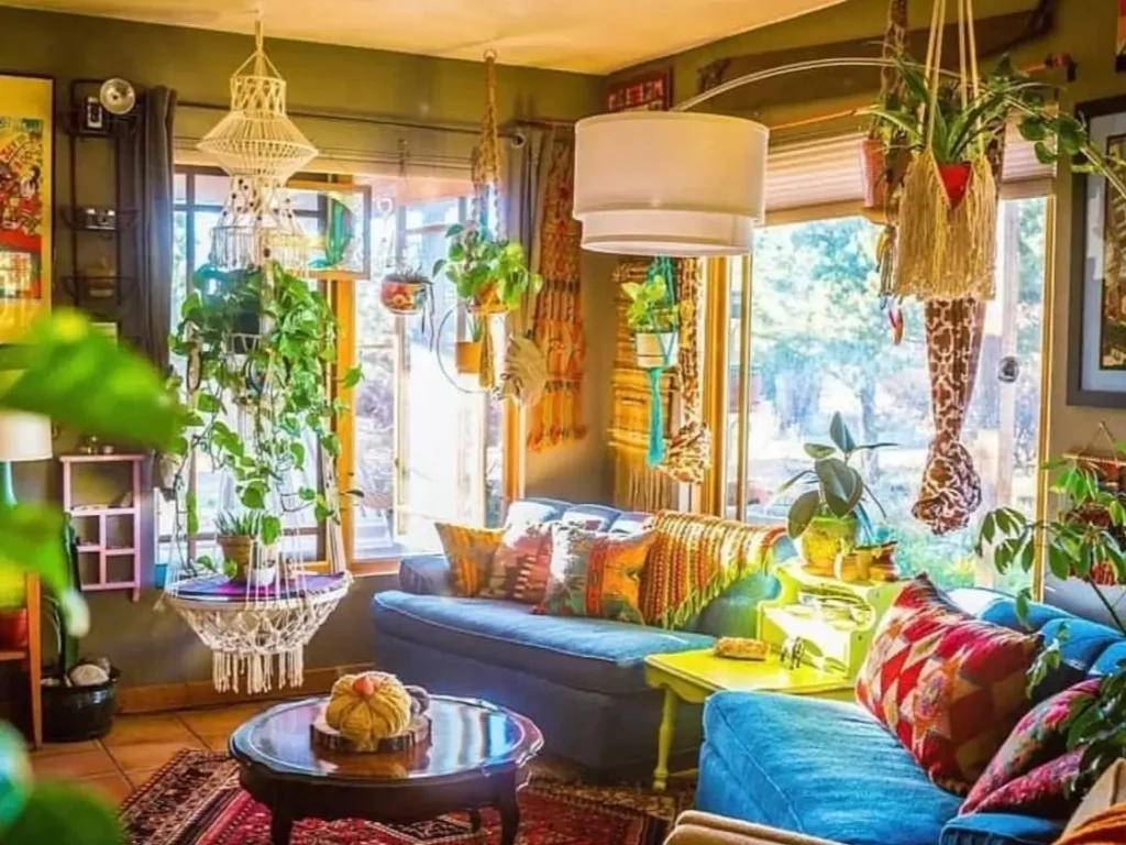 A colorful bohemian living room filled with a blue sofa, numerous patterned pillows, and macrame plant hangers creating a maximalist look.