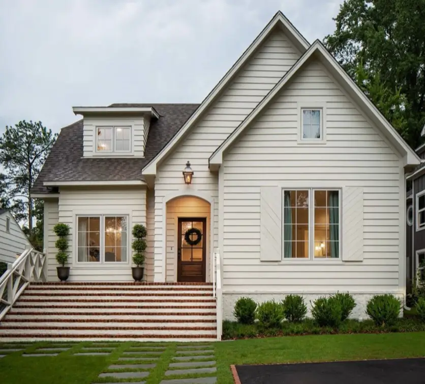 An off-white cottage exterior with a wide brick staircase leading to an arched wooden front door.