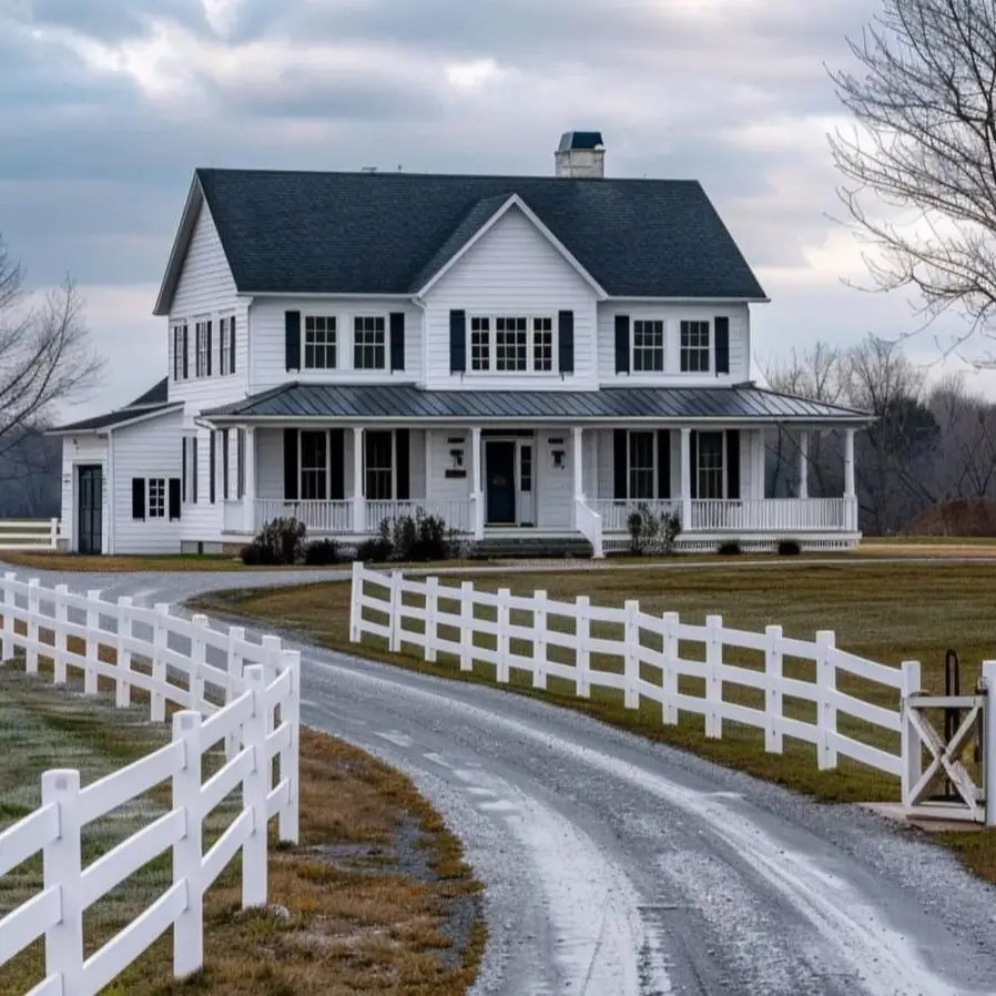 A classic white farmhouse with black shutters, fronted by a long gravel driveway and a traditional white fence.