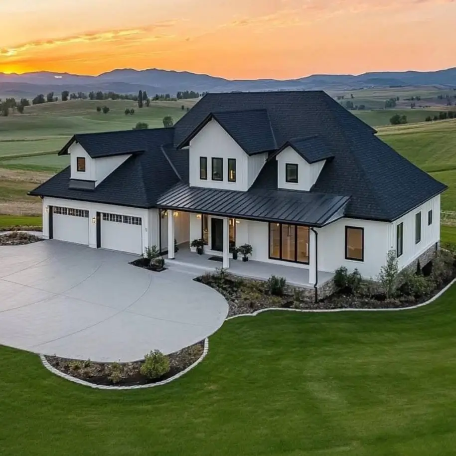 A modern white farmhouse with an integrated three-car garage and a large concrete driveway at sunset.