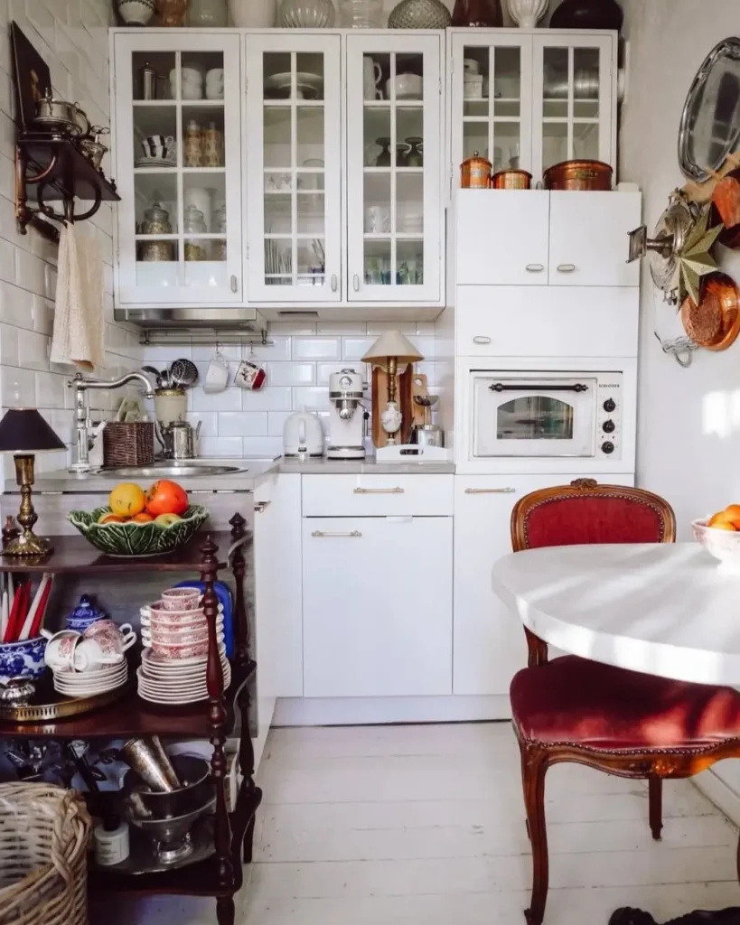 A tiny white kitchen featuring glass-front upper cabinets and vintage-style decor.