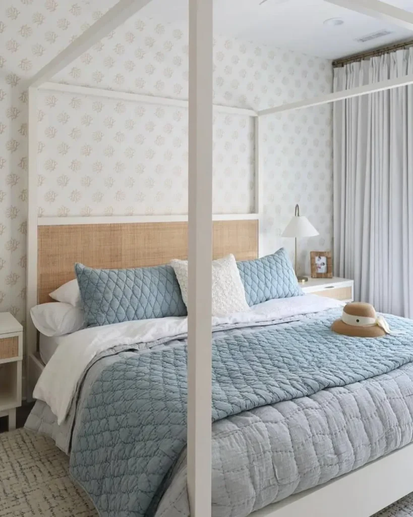 A white canopy bed with a rattan headboard and blue quilted bedding in a serene coastal bedroom.