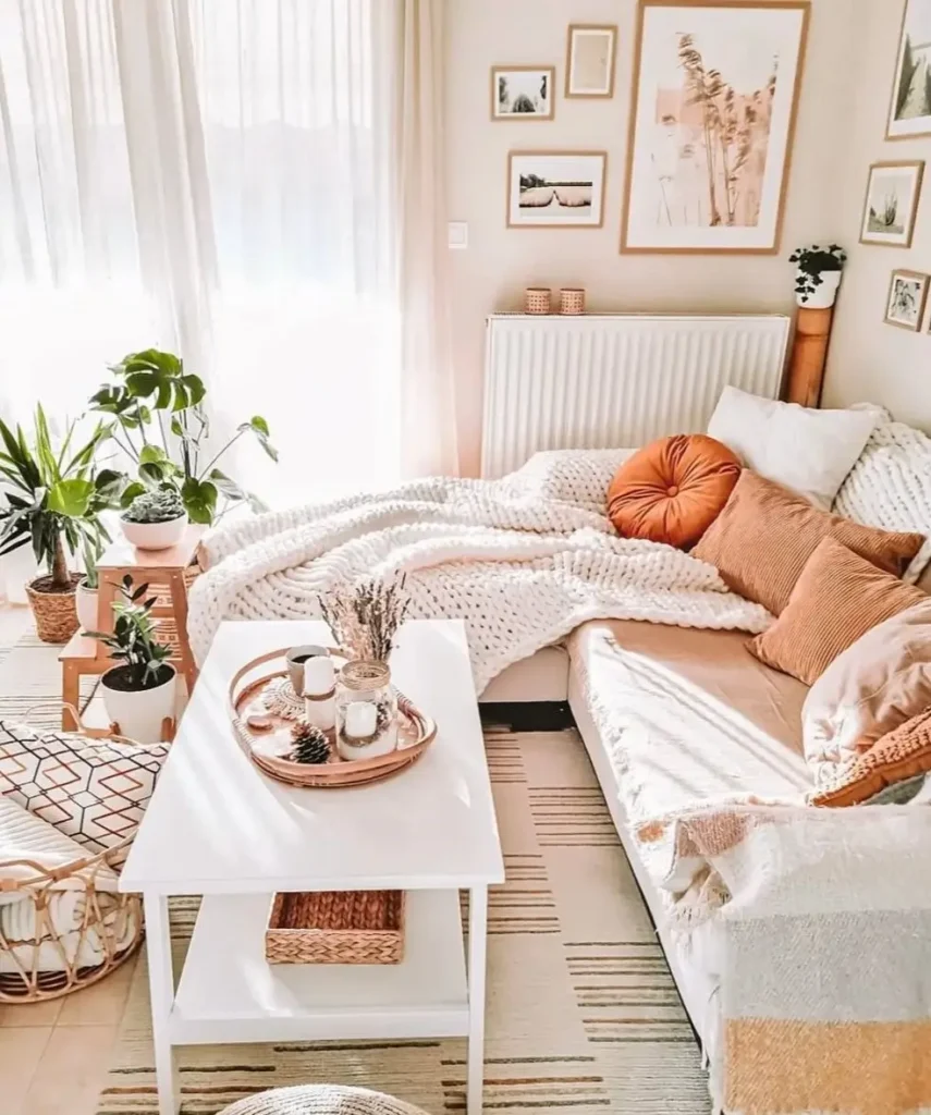 A sunlit and cozy bohemian living room with a beige sofa covered in a chunky white knit blanket and terracotta pillows.