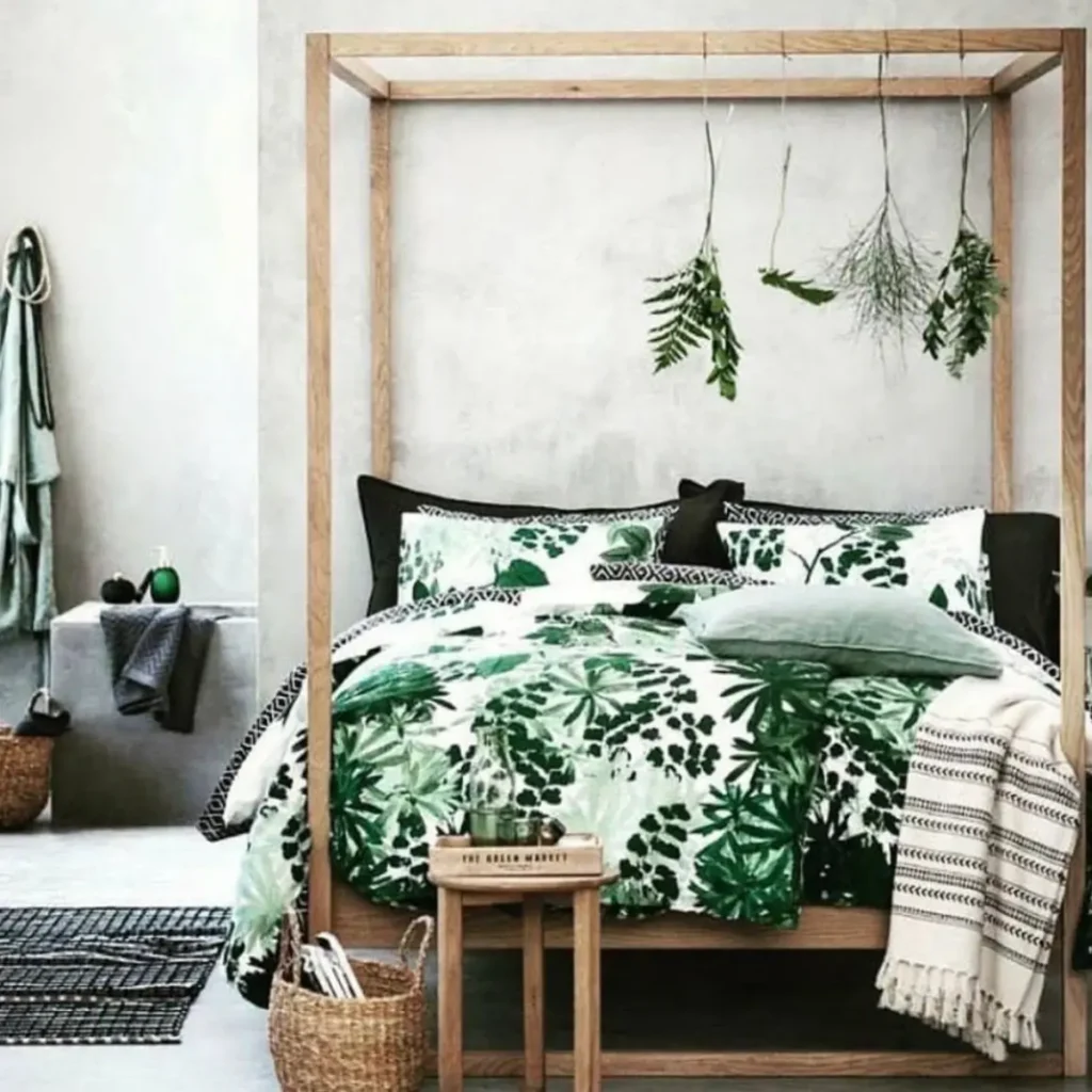 A minimalist bedroom with a wooden four-poster bed, leaf-print bedding, and dried ferns hanging from the canopy.