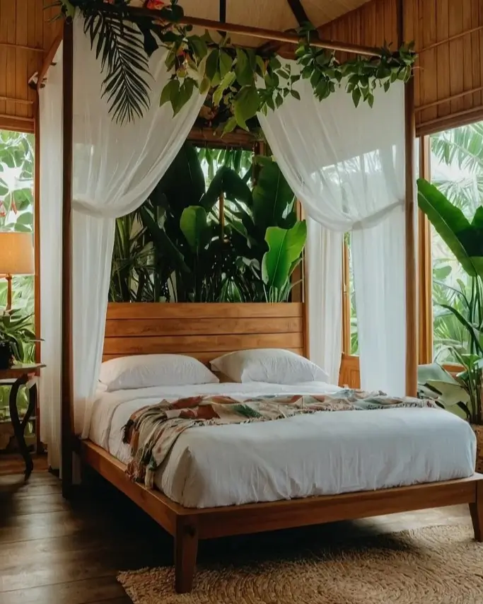 A tropical nature bedroom with a wooden four-poster bed draped in sheer curtains and fresh greenery.