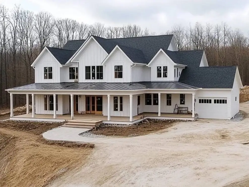 A new modern white farmhouse exterior featuring multiple gables, a dark shingle roof, and a porch with a metal roof.