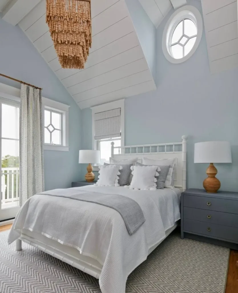 An airy beach themed bedroom with a vaulted shiplap ceiling, a beaded chandelier, and a round porthole window.