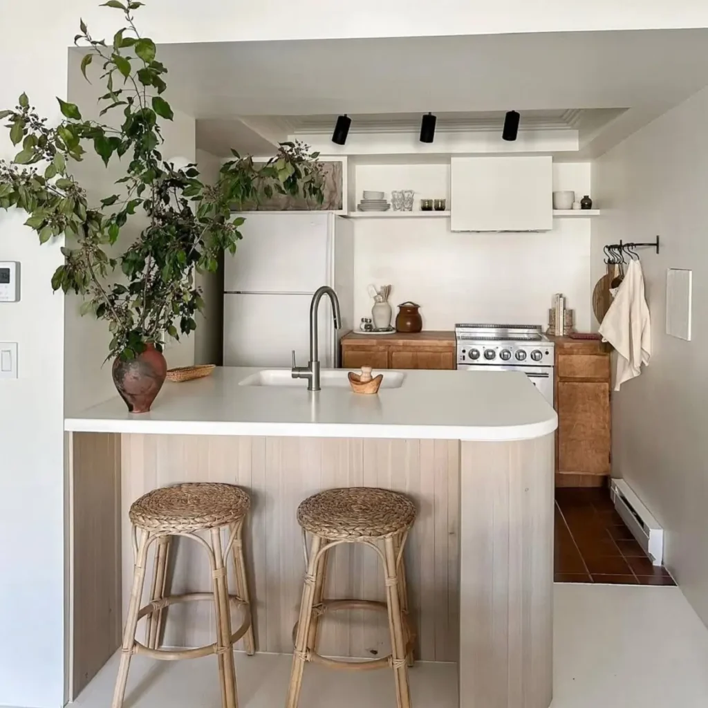 A modern small kitchen with a curved white peninsula, wood cabinets, and rattan stools.