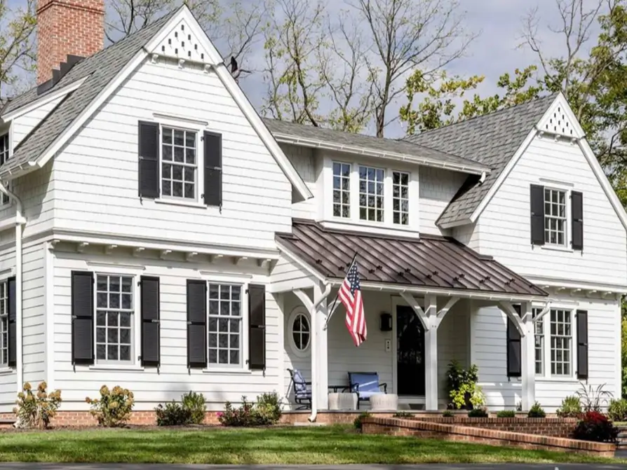 A large white cottage with black shutters, multiple gables, and a dark metal roof over the front porch.