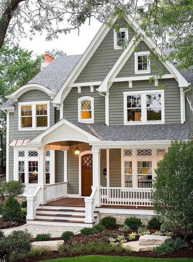 A classic cottage exterior with sage green siding, extensive white trim, a covered front porch, and a natural wood front door.