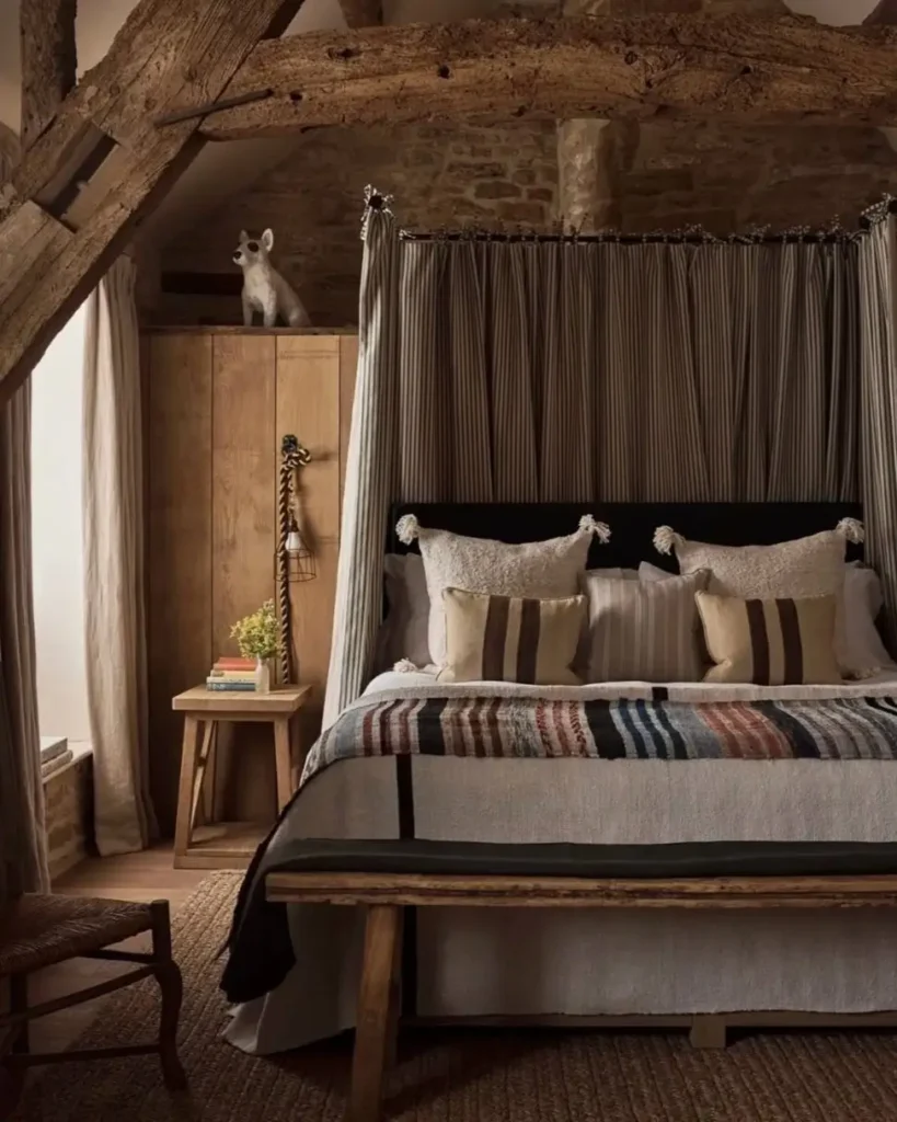 A country rustic bedroom for couples featuring exposed stone walls, dark wood ceiling beams, and a canopy bed with striped fabric.