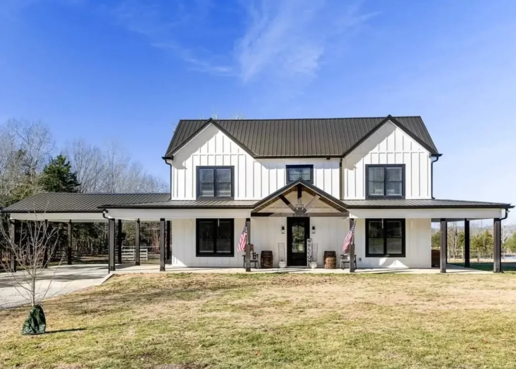 A modern white farmhouse with black trim and a dark metal roof, featuring an attached carport and a welcoming front porch.