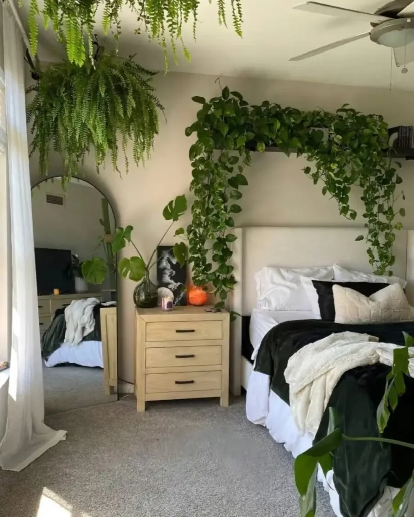 A nature-inspired bedroom featuring a large hanging fern and cascading vines over the headboard, with a floor mirror reflecting the greenery.