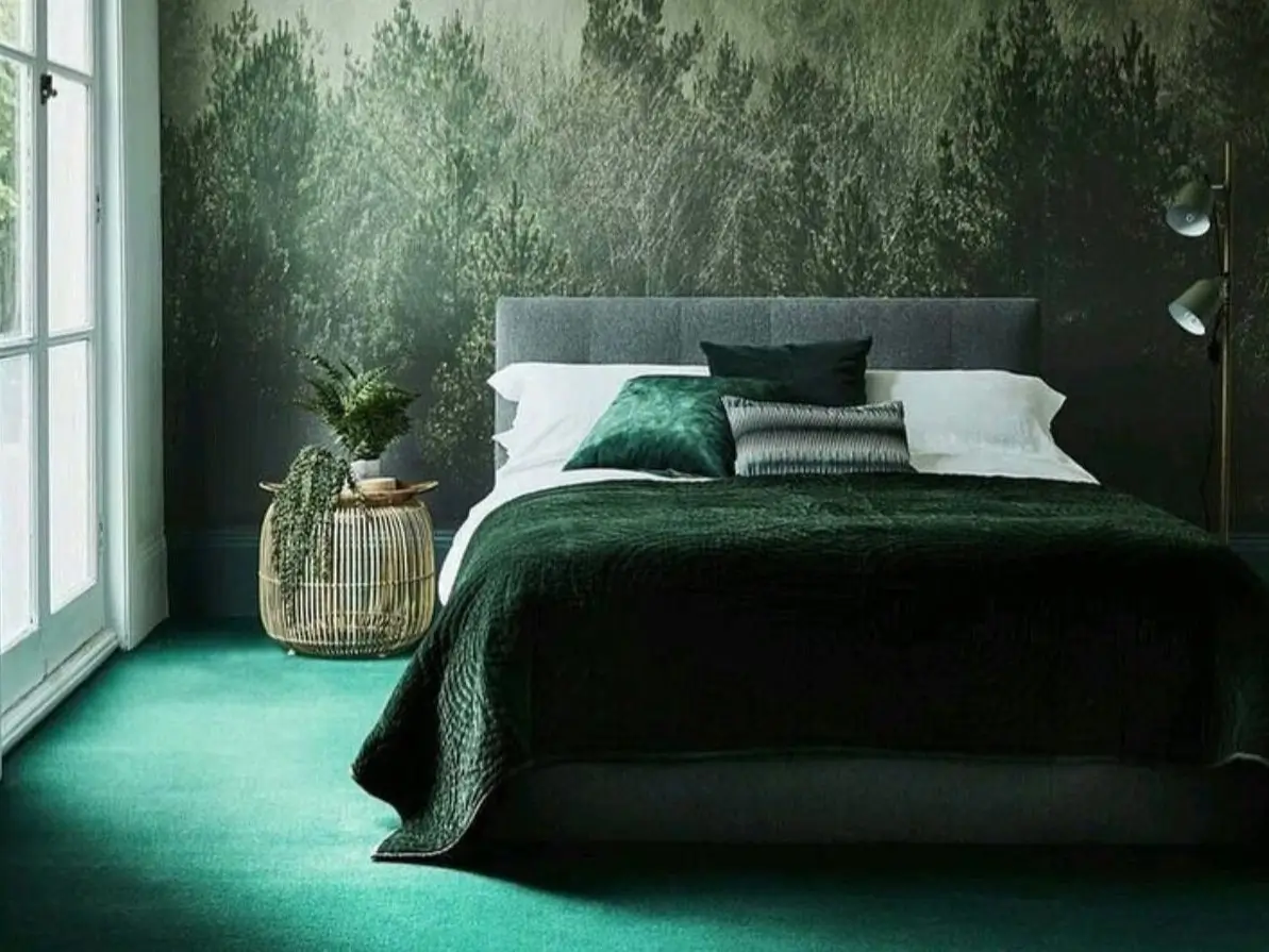 A tranquil nature bedroom design featuring a dark green forest wall mural, a bed with velvet bedding, and a rattan side table.