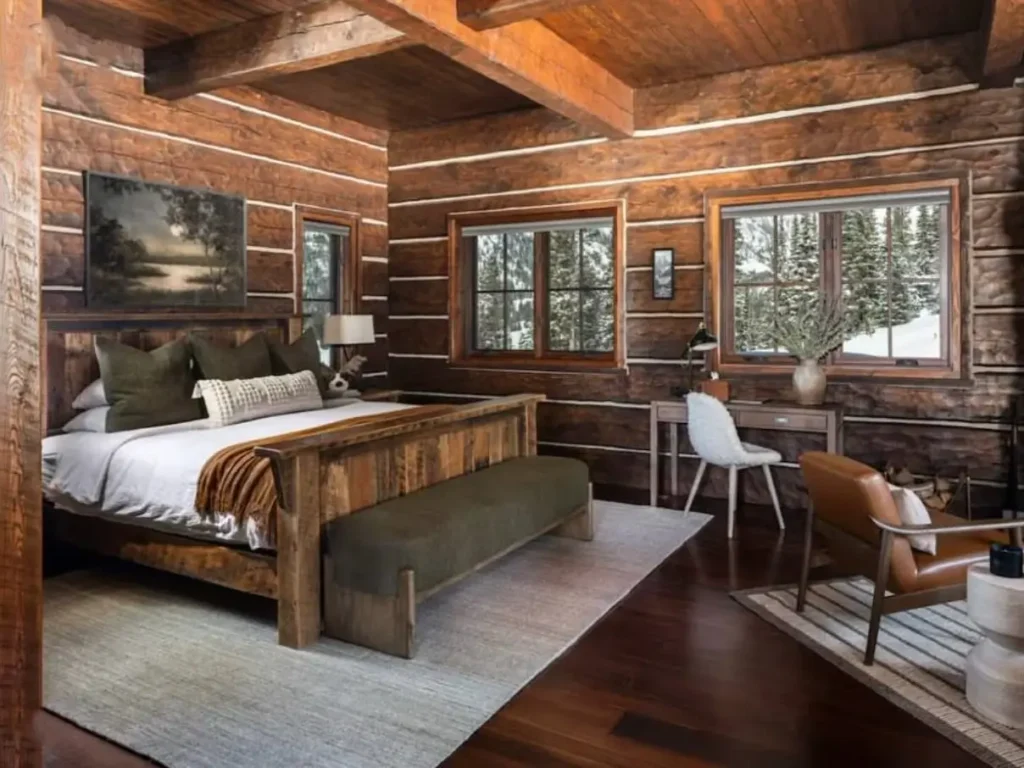 A modern rustic log cabin bedroom for couples, featuring a large wooden bed, dark log walls, and windows with a snowy view.