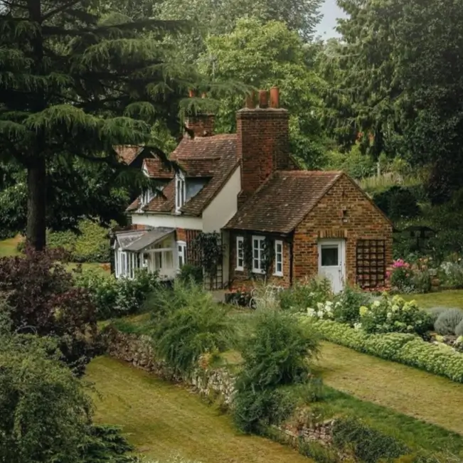 A classic country house design featuring a charming brick cottage surrounded by a lush, sprawling garden.