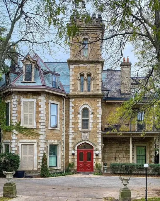 20 Stone Mansion Ideas for Classic & Modern Designs 3 A historic stone mansion featuring a prominent central tower, arched windows, and a bold red double door entrance.