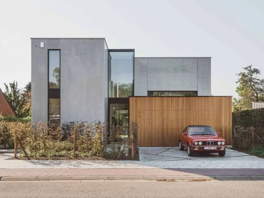 A modern concrete house exterior featuring large windows and a warm wood-paneled garage.