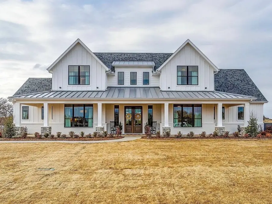 A symmetrical off-white modern farmhouse exterior with a dark metal porch roof and black windows.