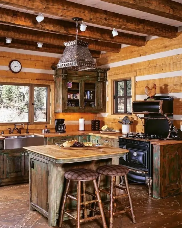 A rustic kitchen design idea featuring log cabin walls, distressed green cabinetry, and a central wooden island with bar stools.