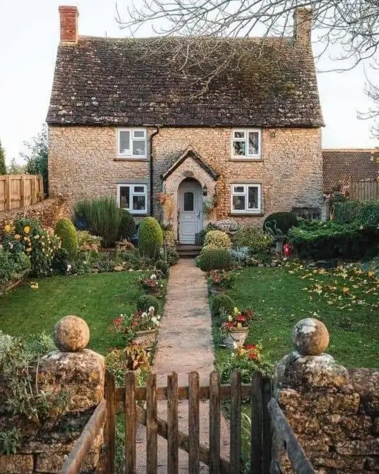 A symmetrical stone cottage house with a lush green garden and a stone path leading to the front door.