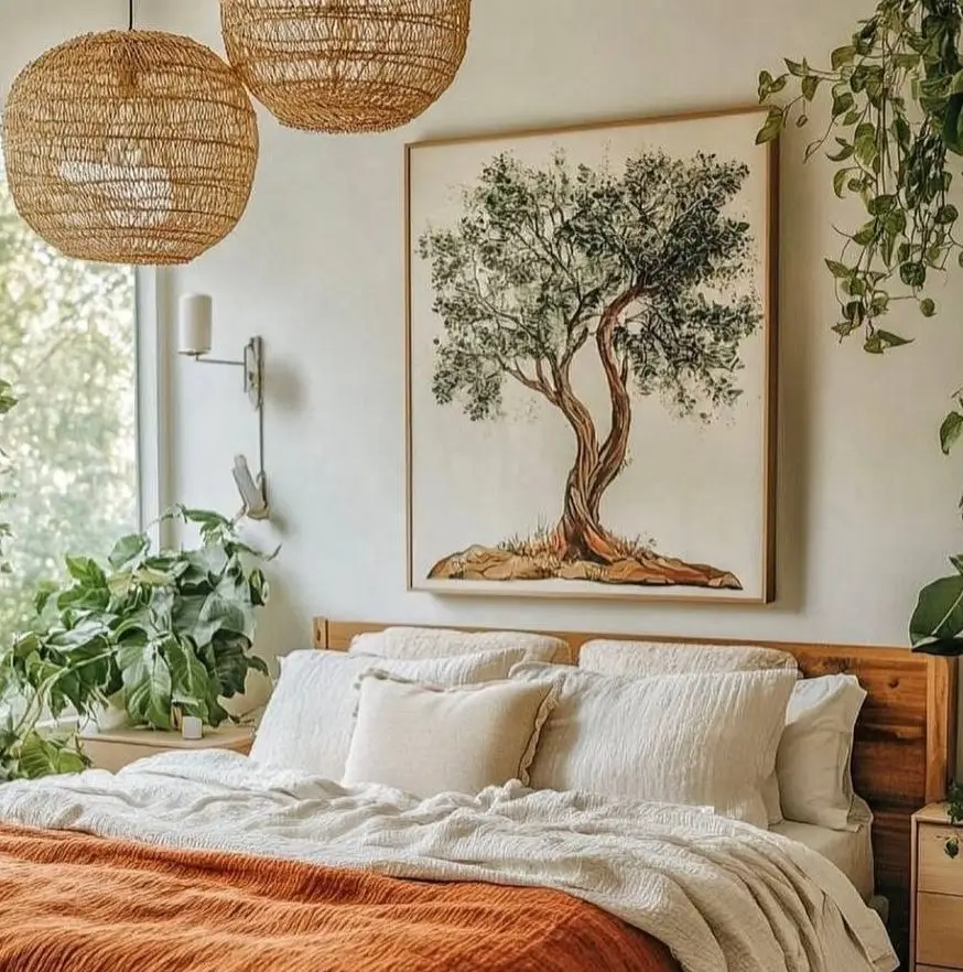 A bright, airy boho bedroom with a large framed print of an olive tree hanging over a bed with rust-colored linens.