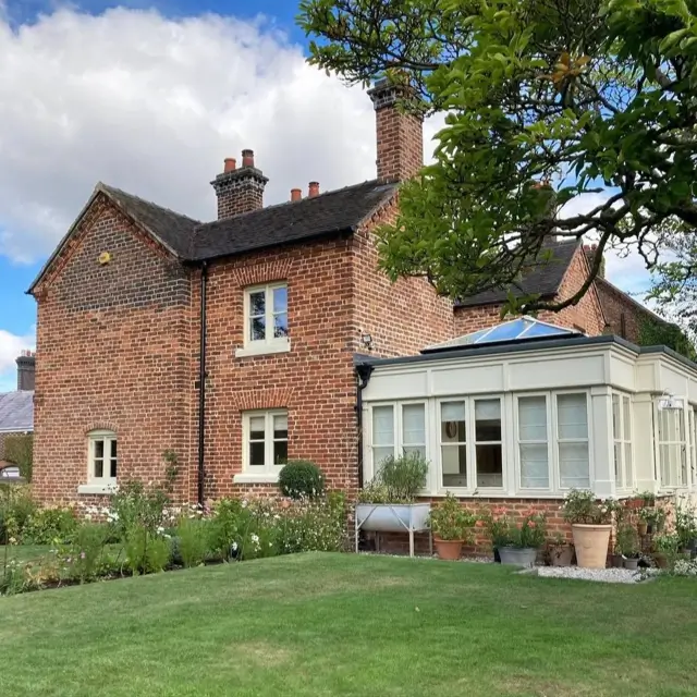 Red brick British country house with an attached white conservatory overlooking a large green lawn.