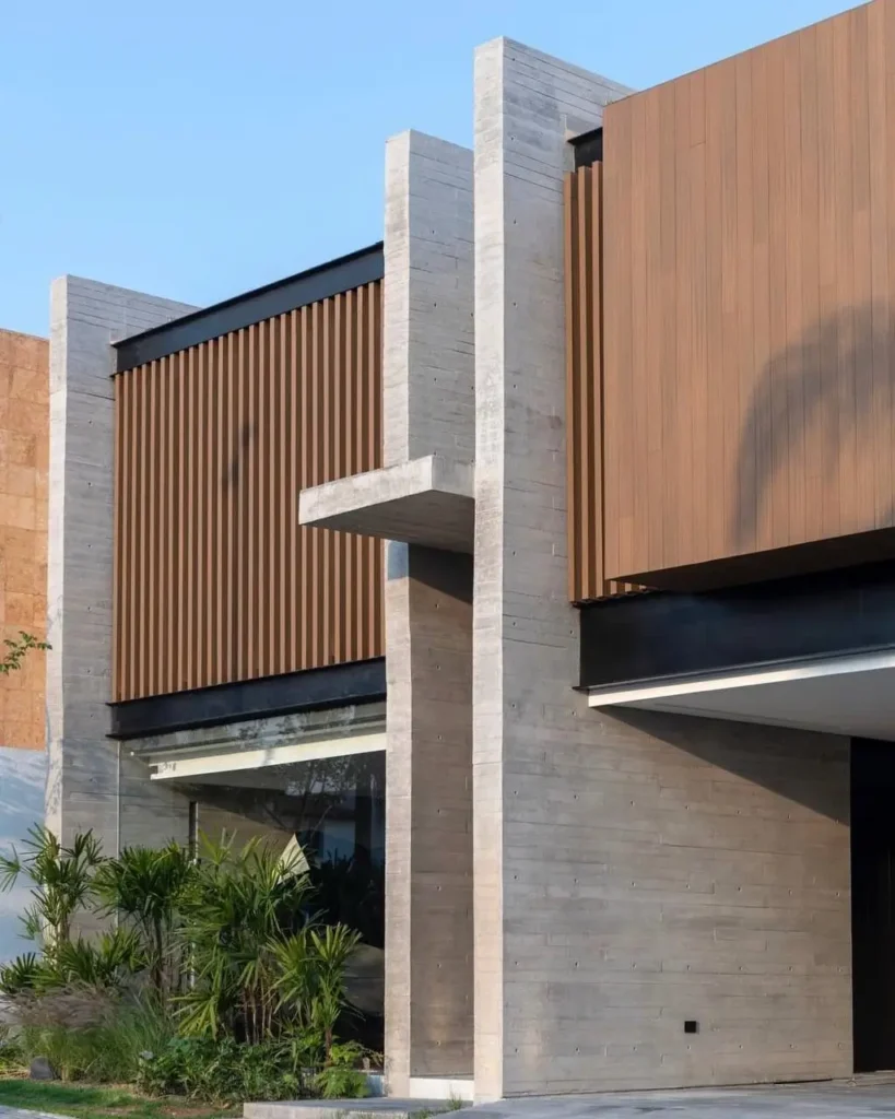 The exterior of a contemporary concrete home featuring prominent structural fins framing inset wood paneling.