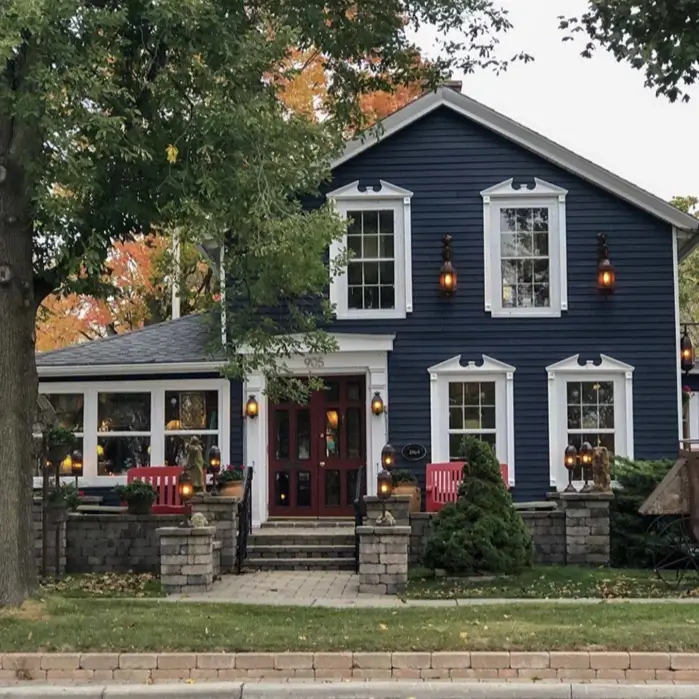A classic country house design with dark blue siding, featuring ornate white trim around the windows and a red door.