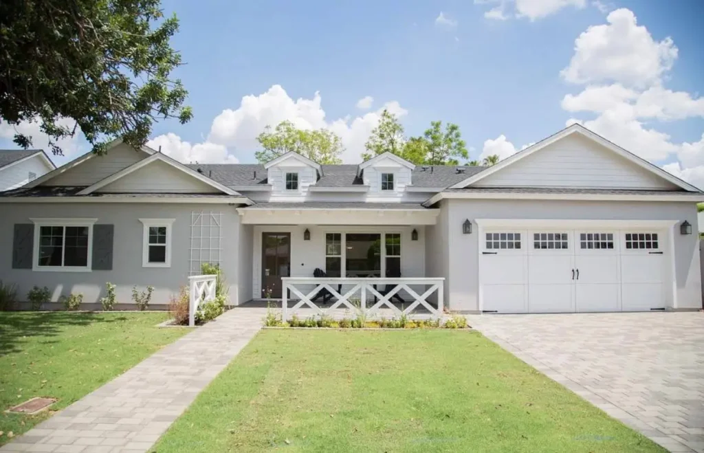 A light gray ranch house with white trim, dormer windows, and a farmhouse-style front porch.