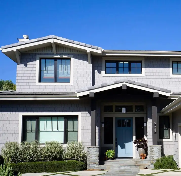 A modern craftsman house exterior with cool gray shingle siding, dark trim, and a welcoming light blue front door.