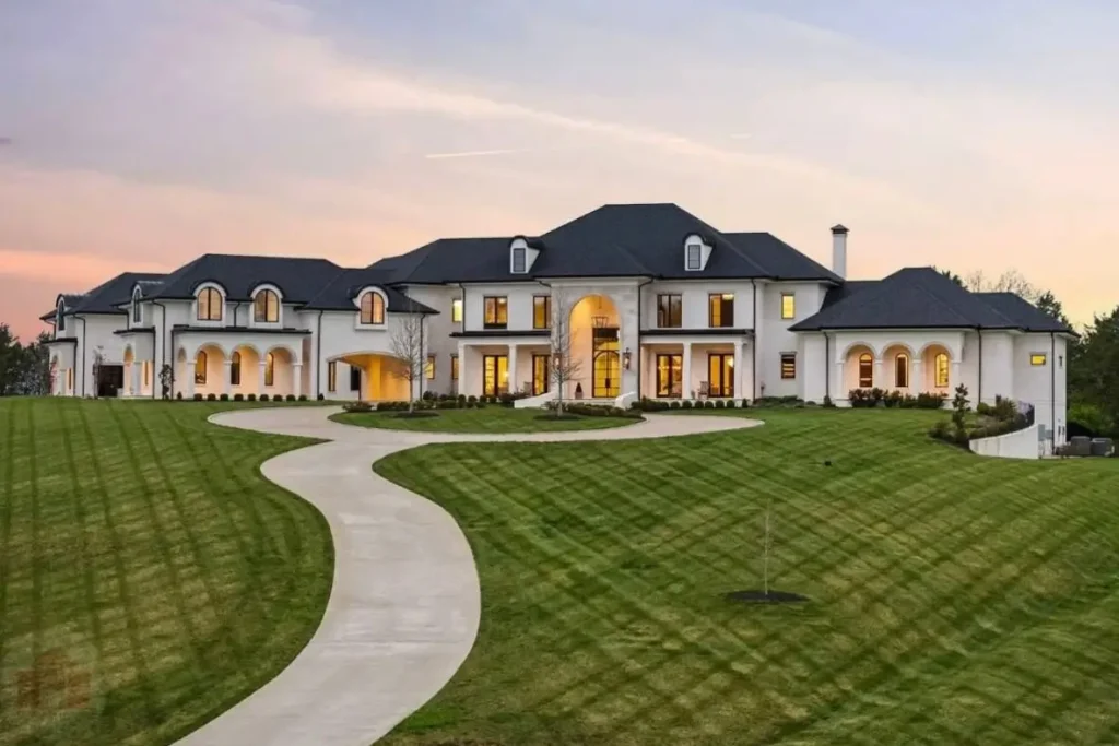 The Ultimate Guide to Luxury Mansion Design: 33 Ideas for Grandeur 13 A sprawling white mansion with a simple, sweeping driveway across a vast lawn at dusk.