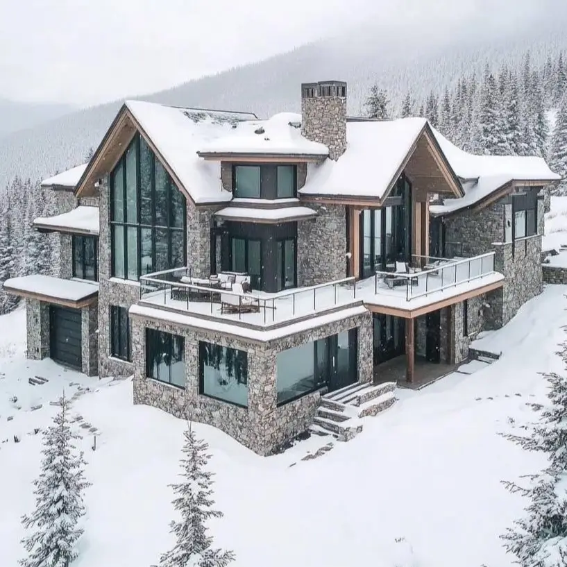 16 Mountain Mansions That Define Luxury Alpine Living 14 The strong, fortress-like silhouette of a modern stone mountain mansion with dark-framed windows, standing out against a deep snowy landscape.